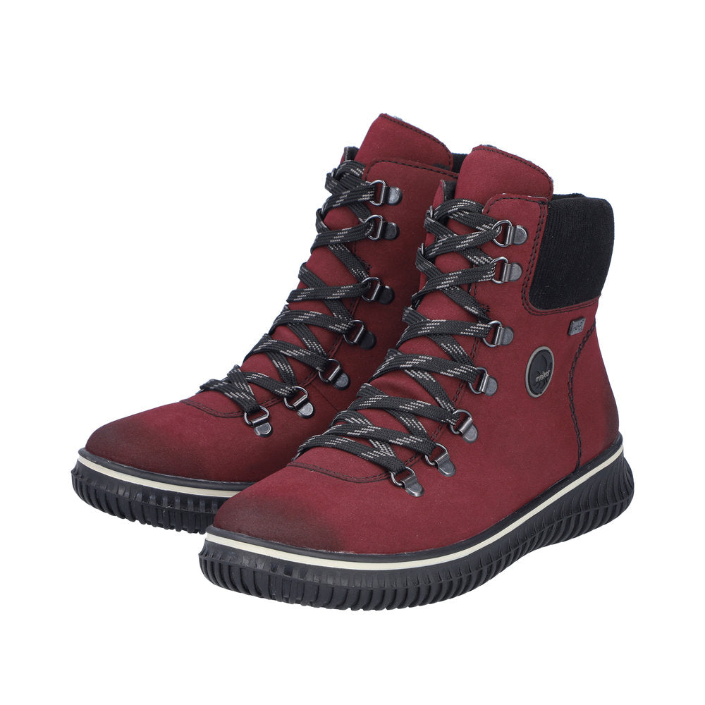 A pair of red ankle high boots with black and white striped laces, metal eyelets and a thick black sole.
