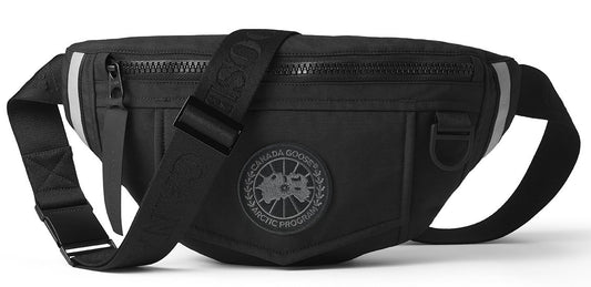 Black fabric belt bag with a circular patch logo, a zipper on top, and an adjustable strap.