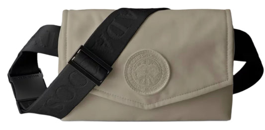 A tan bag with a black strap and a round emblem.