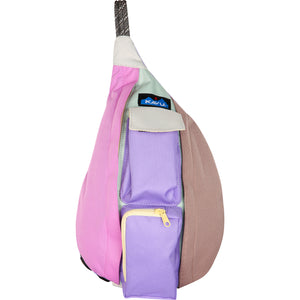 Sling bag with pink, lavender, beige, and light green panels, two lavender front pockets, and the Kavu logo near the strap.