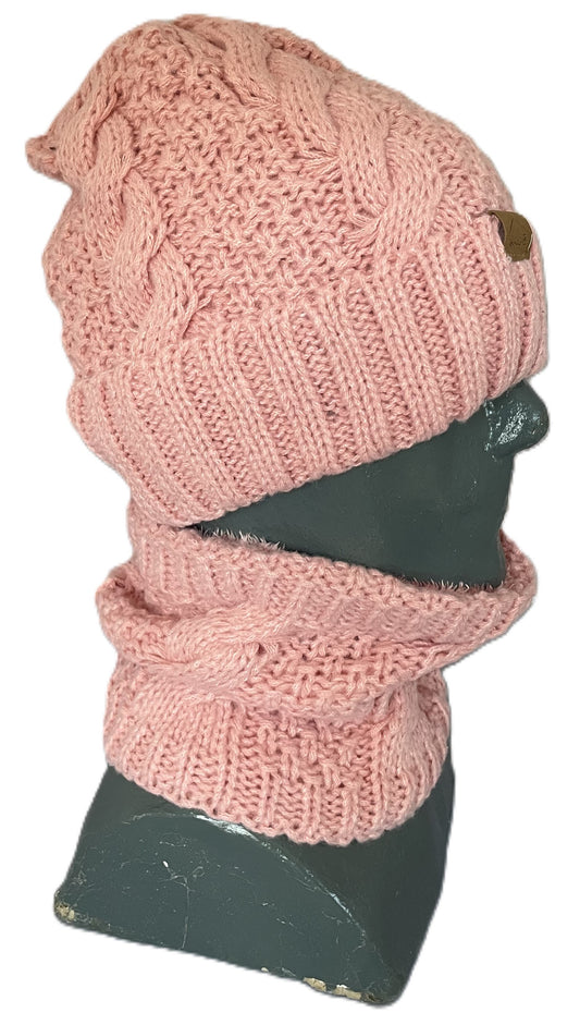 A light pink knit hat and matching cowl scarf set displayed on a dark grey mannequin head, featuring a chunky cable-knit pattern and a small leather-like patch on the hat.