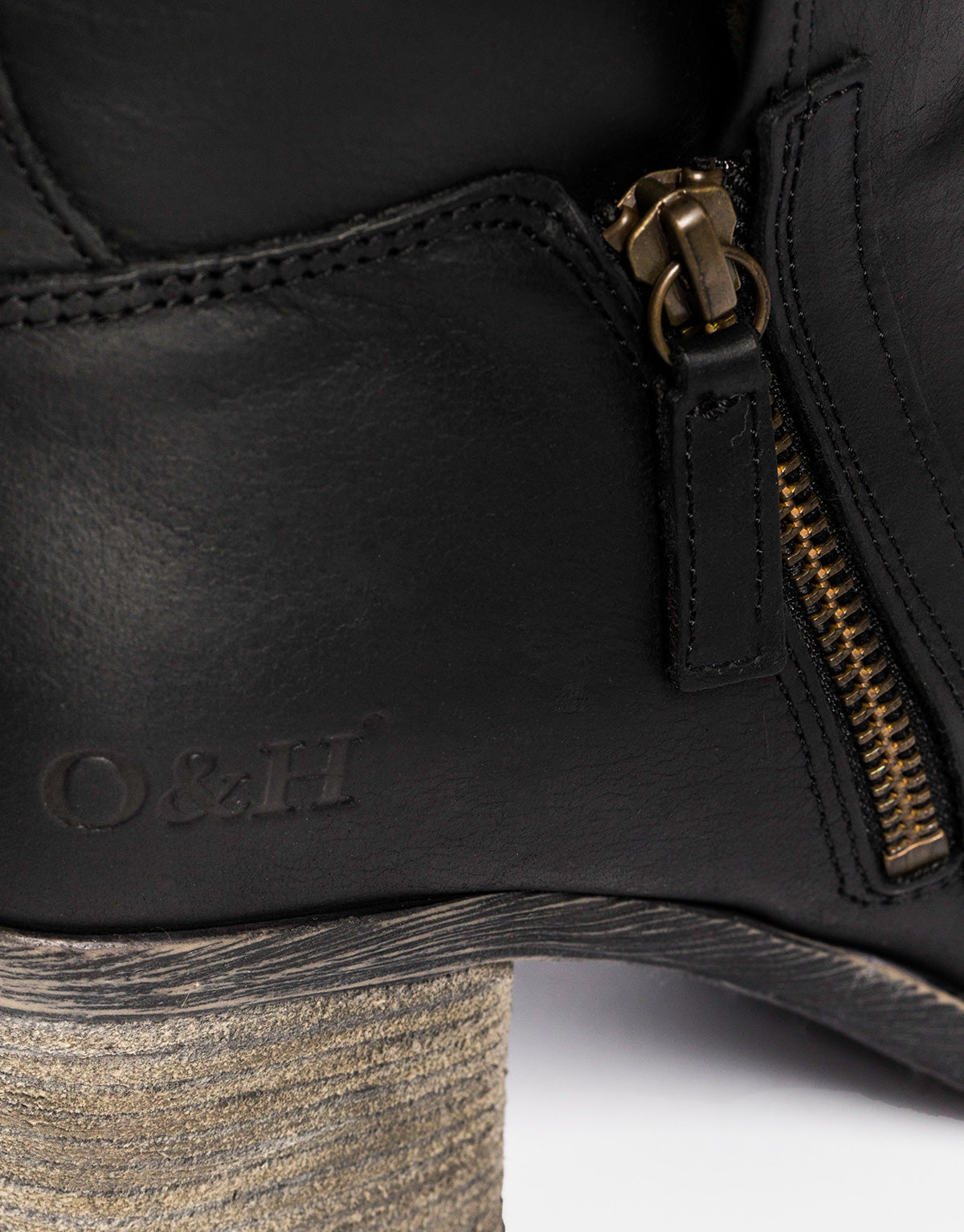 Closeup of a black boot showing a zipper closure and the letters O & H.