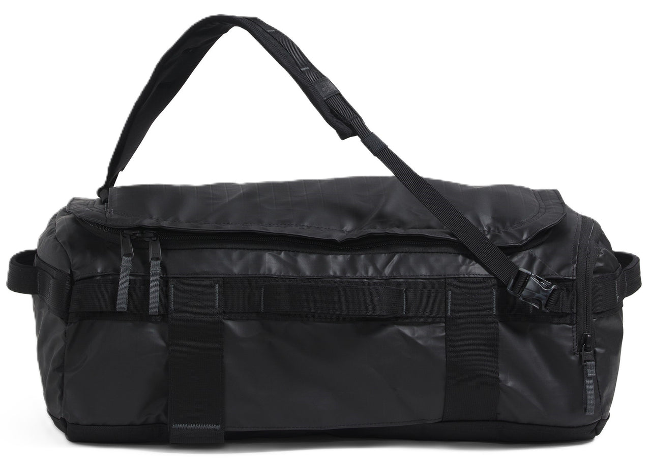 A black duffel bag with a shoulder strap is lying down.