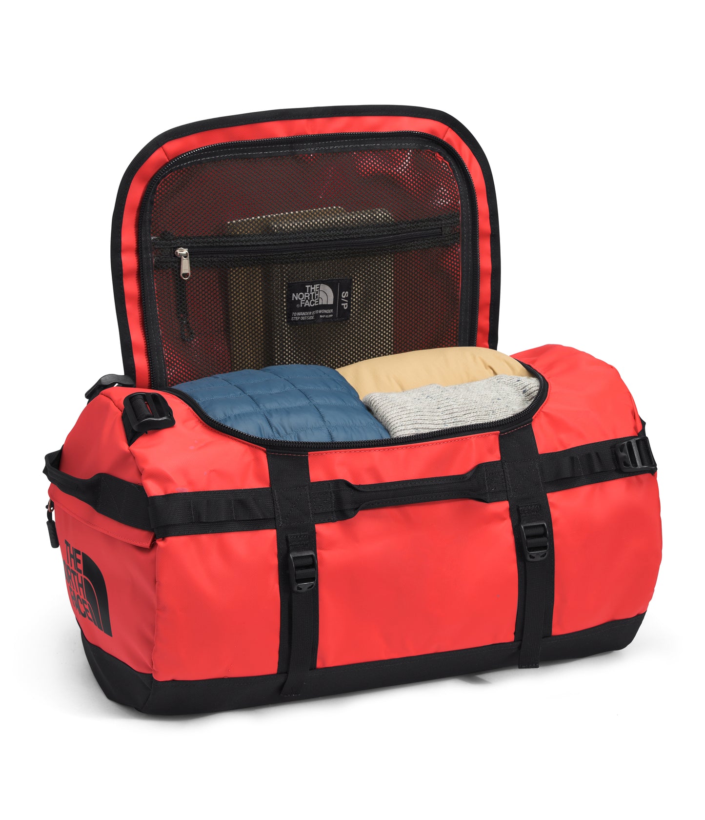 An open red duffel bag with black straps and bottom, revealing folded clothing and a mesh compartment with a logo.