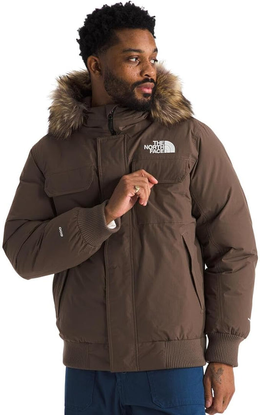 A man with a beard wears a brown puffer jacket with a fur-trimmed hood. "THE NORTH FACE" logo is on the upper chest.