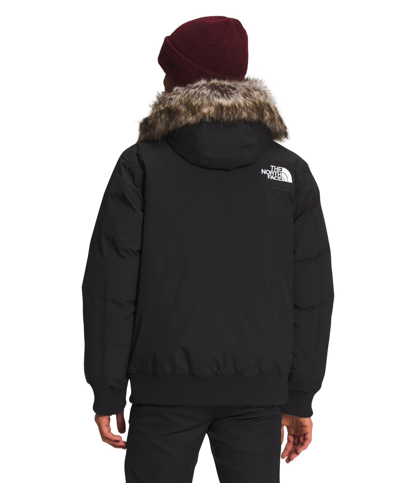 Person wearing black winter jacket with fur hood and maroon beanie, back view.