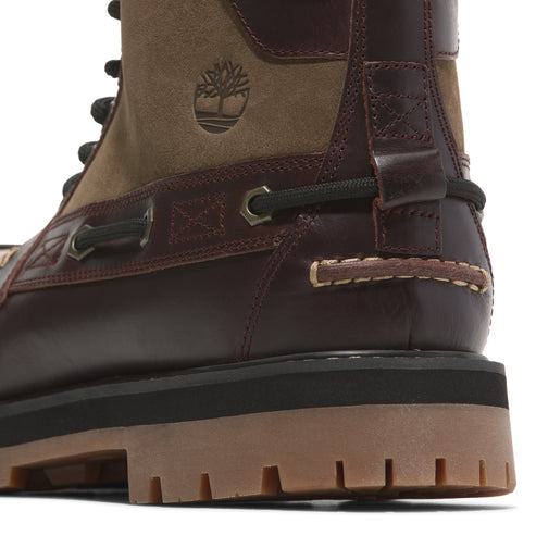 Close-up of a brown boot with a tan suede upper section, a Timberland tree logo, and black laces.