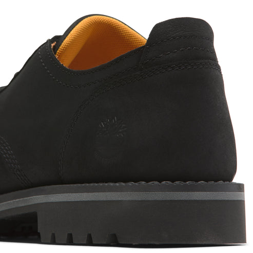 Close-up of a matte black leather dress shoe with a lug sole and a mustard yellow inner lining.