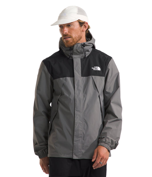A man wearing a gray and black hooded jacket with a white logo on the chest and a white hat.
