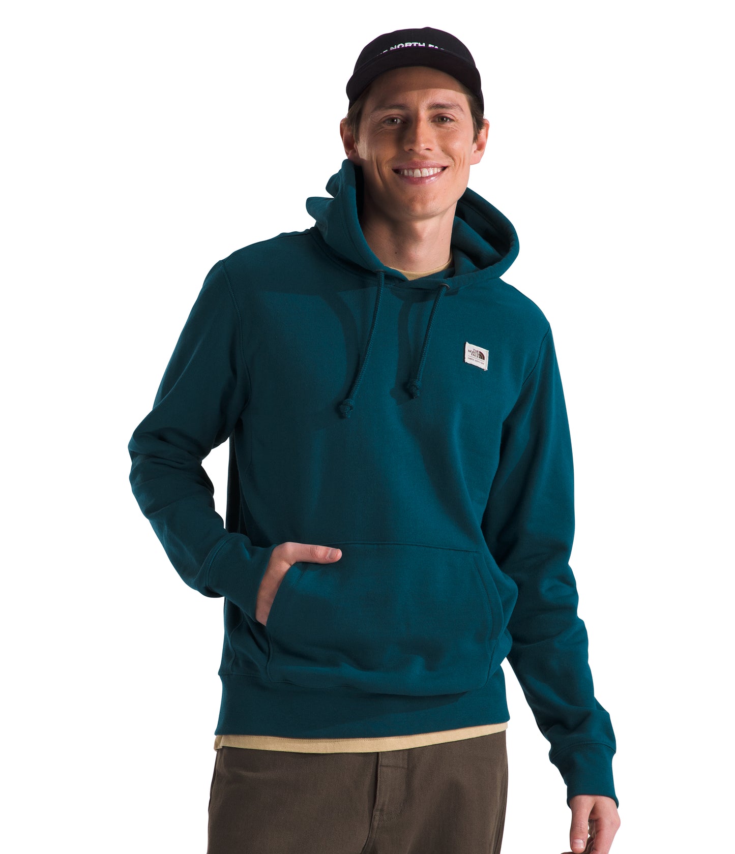 Man in a teal hooded sweatshirt and a black baseball cap, with his hand in the kangaroo pocket.