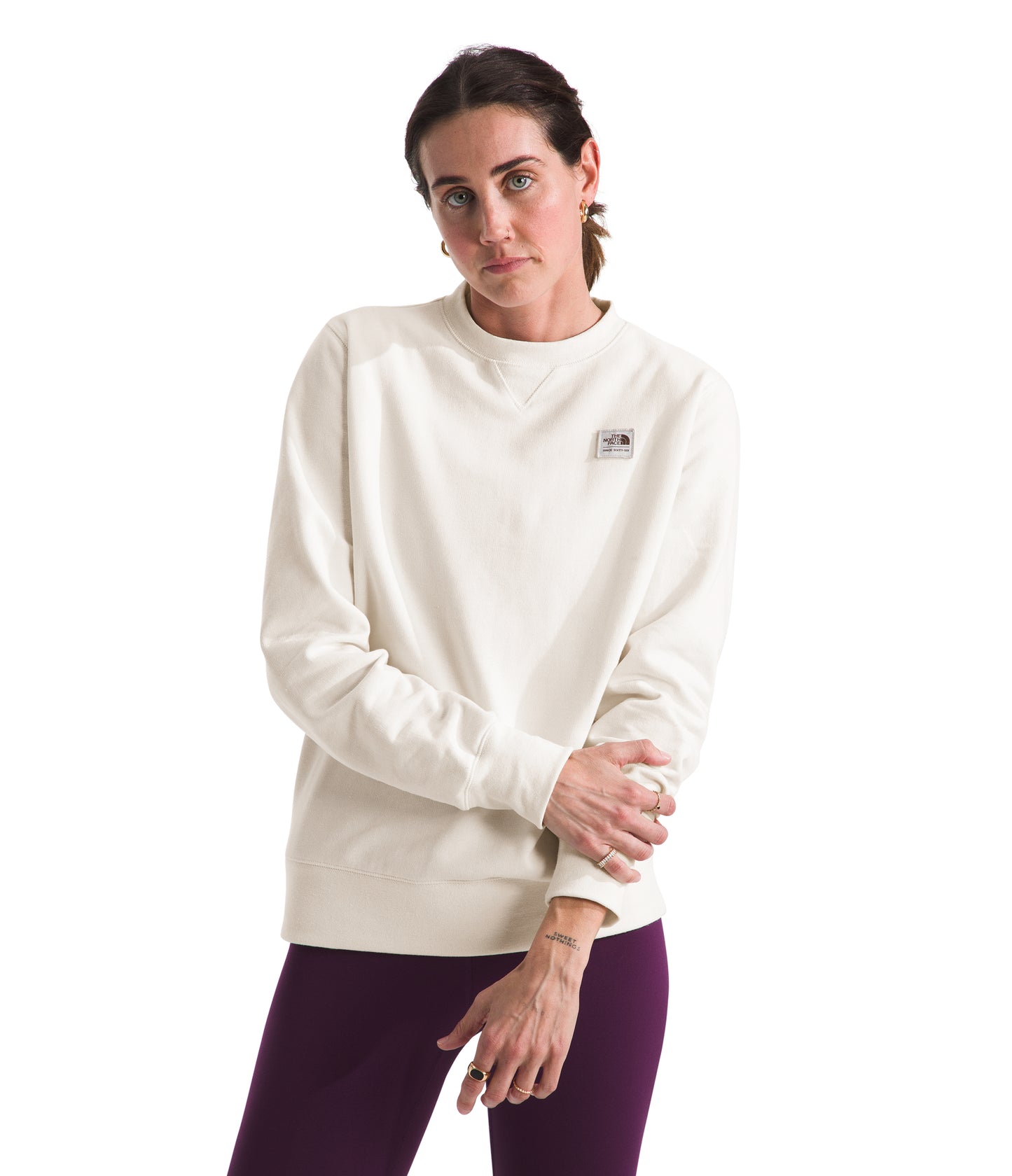 Woman wearing a long-sleeved, solid cream sweatshirt with a small logo on the chest and maroon pants.