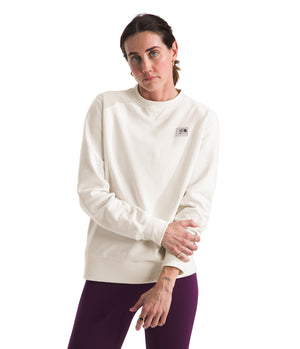 Woman wearing a long-sleeved, solid cream sweatshirt with a small logo on the chest and maroon pants.