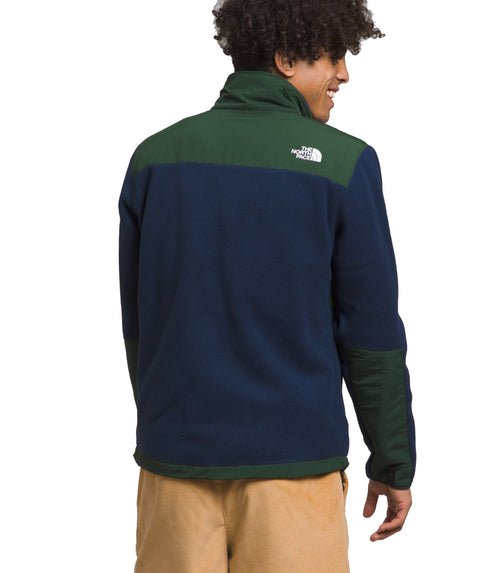 Man wearing a color-blocked fleece jacket in navy, forest green, and tan pants. The jacket has a high collar and a small logo on the upper back.