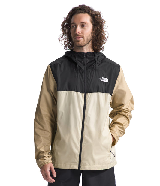 A man wearing a hooded two tone jacket. The top is black and the bottom is tan.