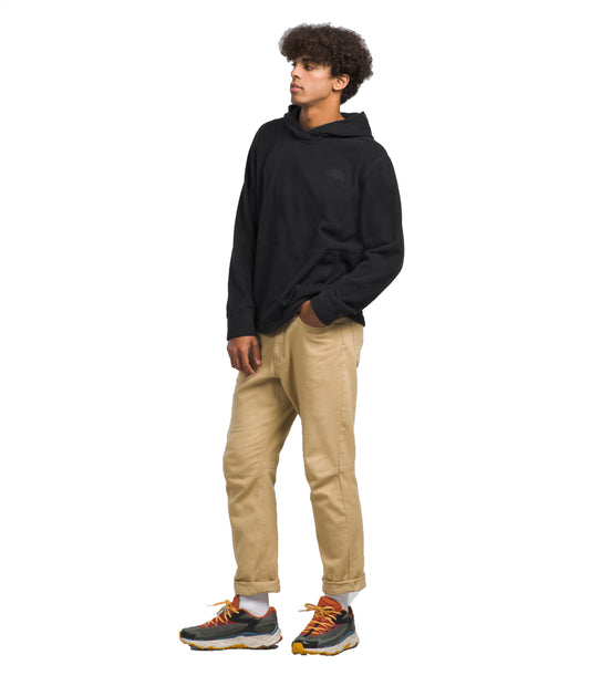 A person in a black long sleeve hooded shirt and tan pants and athletic shoes looks to the left.