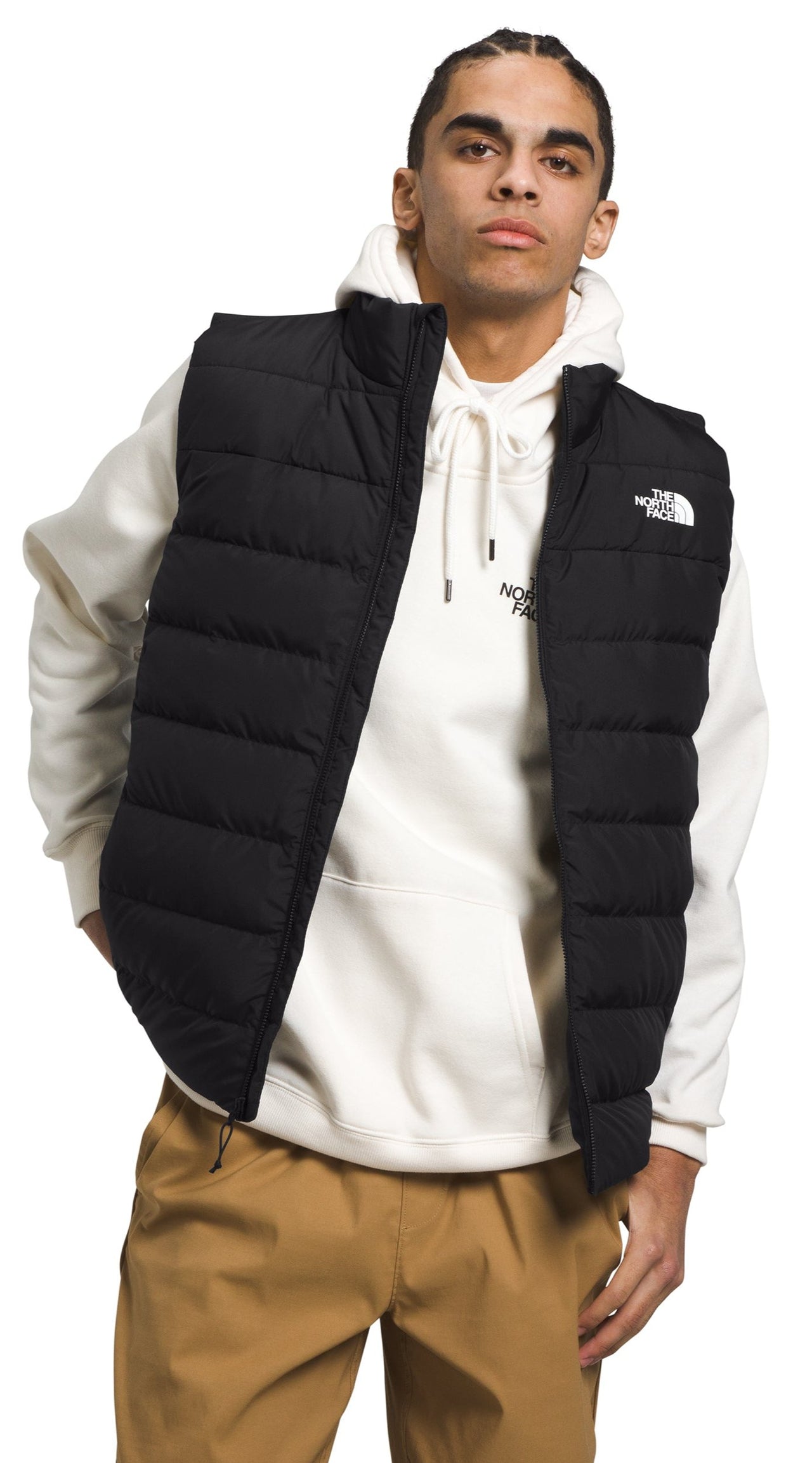 A man wearing a black puffer vest over a cream colored hoodie and khaki pants.