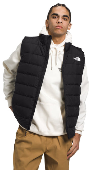 A man wearing a black puffer vest over a cream colored hoodie and khaki pants.