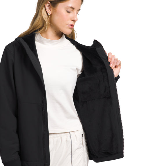 A blonde woman is wearing a black hooded jacket and a white turtleneck, with the jacket open to reveal a large inside pocket.