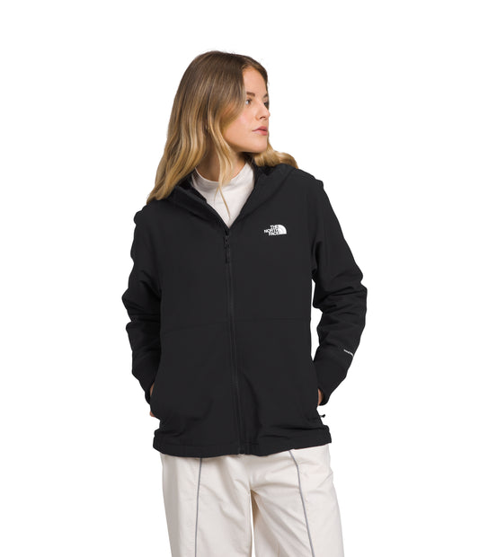 A person with long hair wears a black, zippered jacket over a white shirt and light-colored pants.