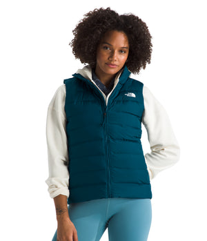 A woman wearing a teal, zip-up vest over a cream-colored hoodie and light blue leggings.
