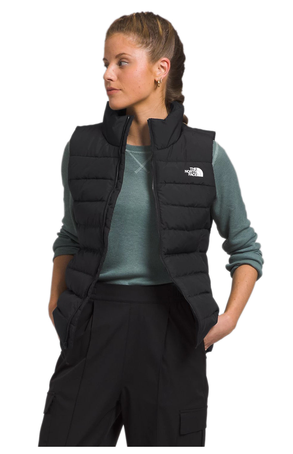A woman wears a black puffer vest over a teal shirt.