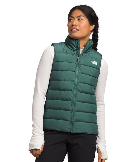 A woman wearing a puffy green zip-up vest over a white long-sleeved shirt with black pants.