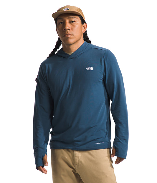 A person wearing a long-sleeved blue hooded shirt with a white logo on the upper chest and a tan hat.