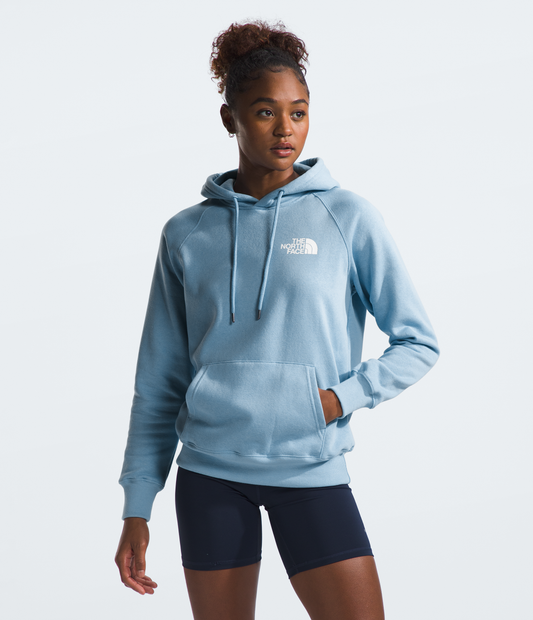 Woman in light blue hoodie with white logo and dark shorts, standing.