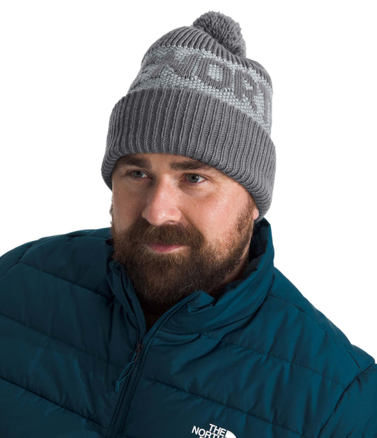Man wearing gray beanie with a pom on top and a blue puffy jacket.