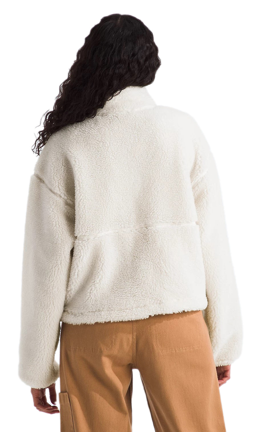 A woman with curly dark hair wears a white fleece jacket and brown pants. The back of the jacket has a horizontal seam.
