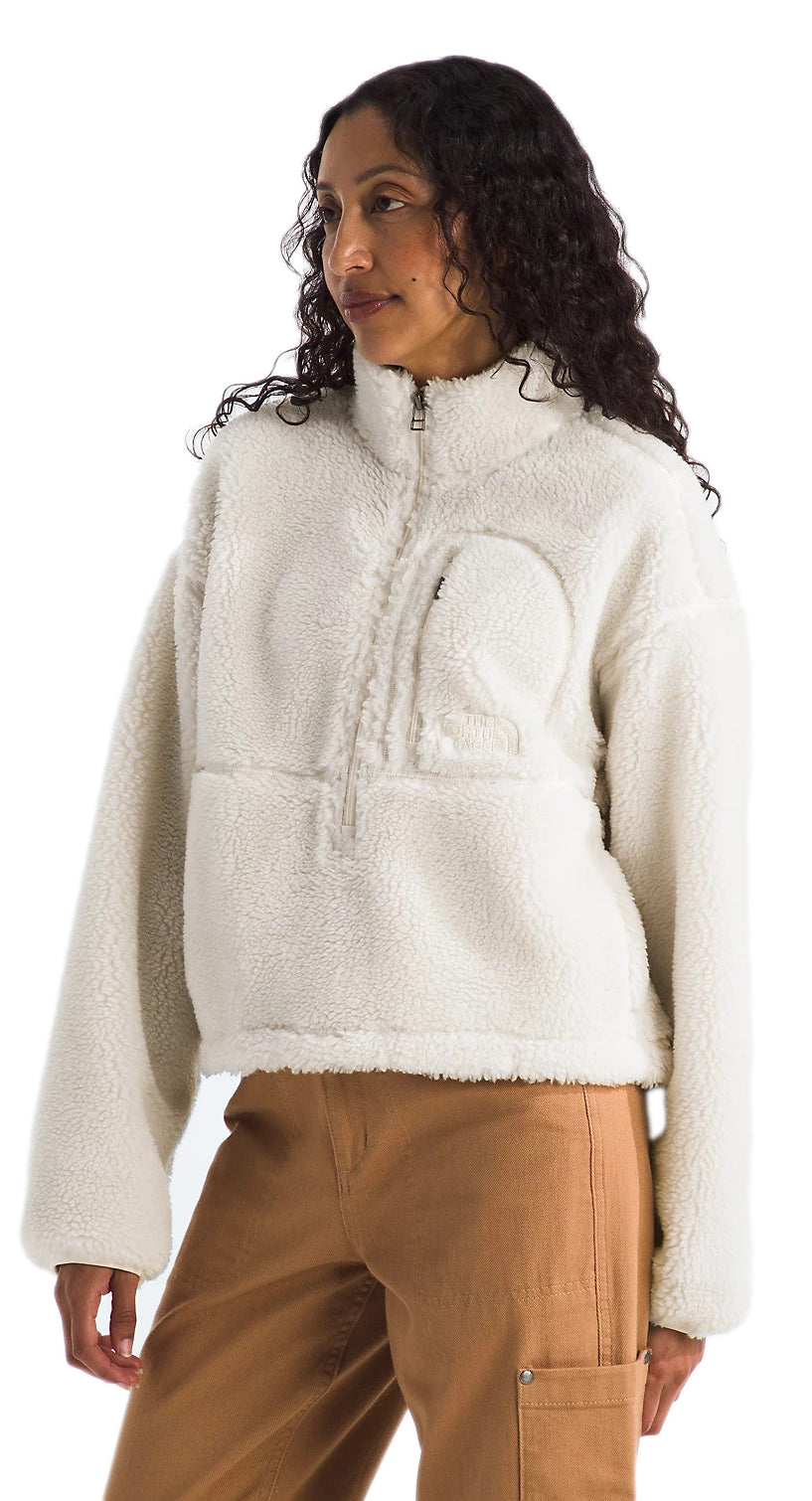 A woman wearing a long-sleeve, off-white, faux fur pullover with a quarter zip at the neck and a pocket on the chest, posing against a white background.