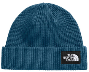 Close-up of a teal knit beanie with a black patch displaying a white, stylized quarter-circle and text: "THE NORTH FACE".