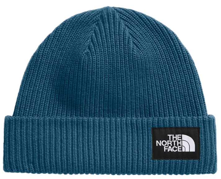 Close-up of a teal knit beanie with a black patch displaying a white, stylized quarter-circle and text: "THE NORTH FACE".