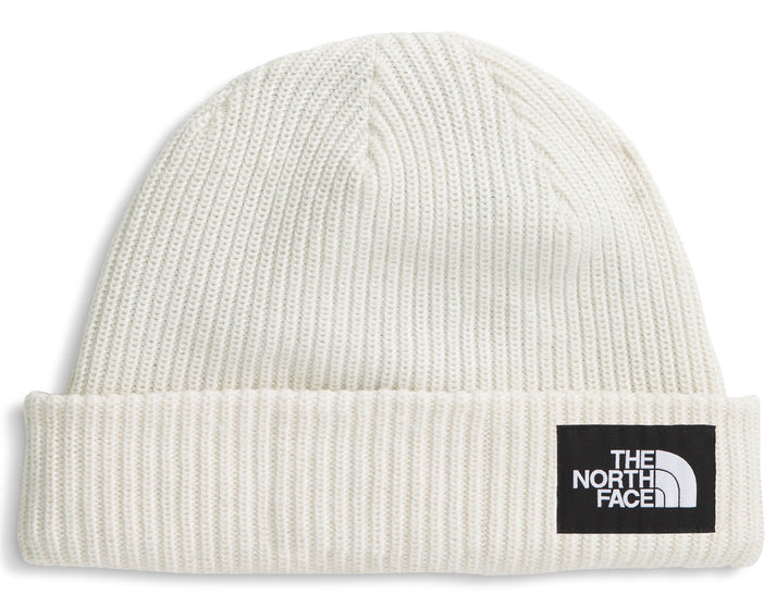 Close-fitting off-white knit hat with a black rectangular patch displaying the words 'THE NORTH FACE' stacked above a quarter circle shape.