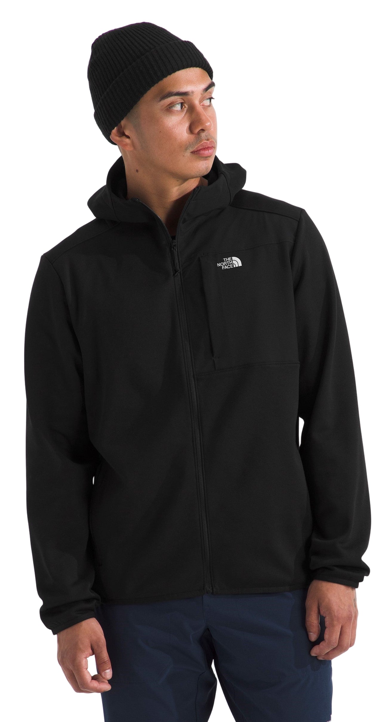 A man wearing a black hooded jacket with a small logo on the upper chest and a black beanie.