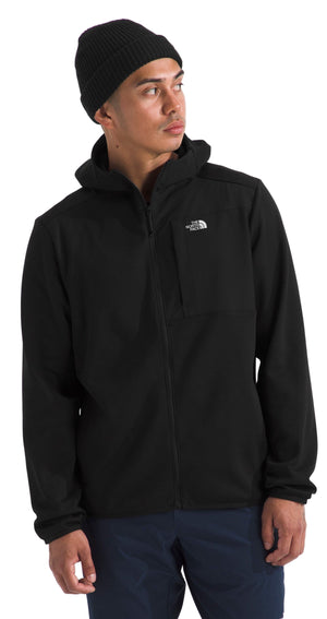 A man wearing a black hooded jacket with a small logo on the upper chest and a black beanie.