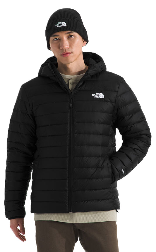 A person wearing a black beanie and a black hooded puffer jacket with a white logo on the chest.