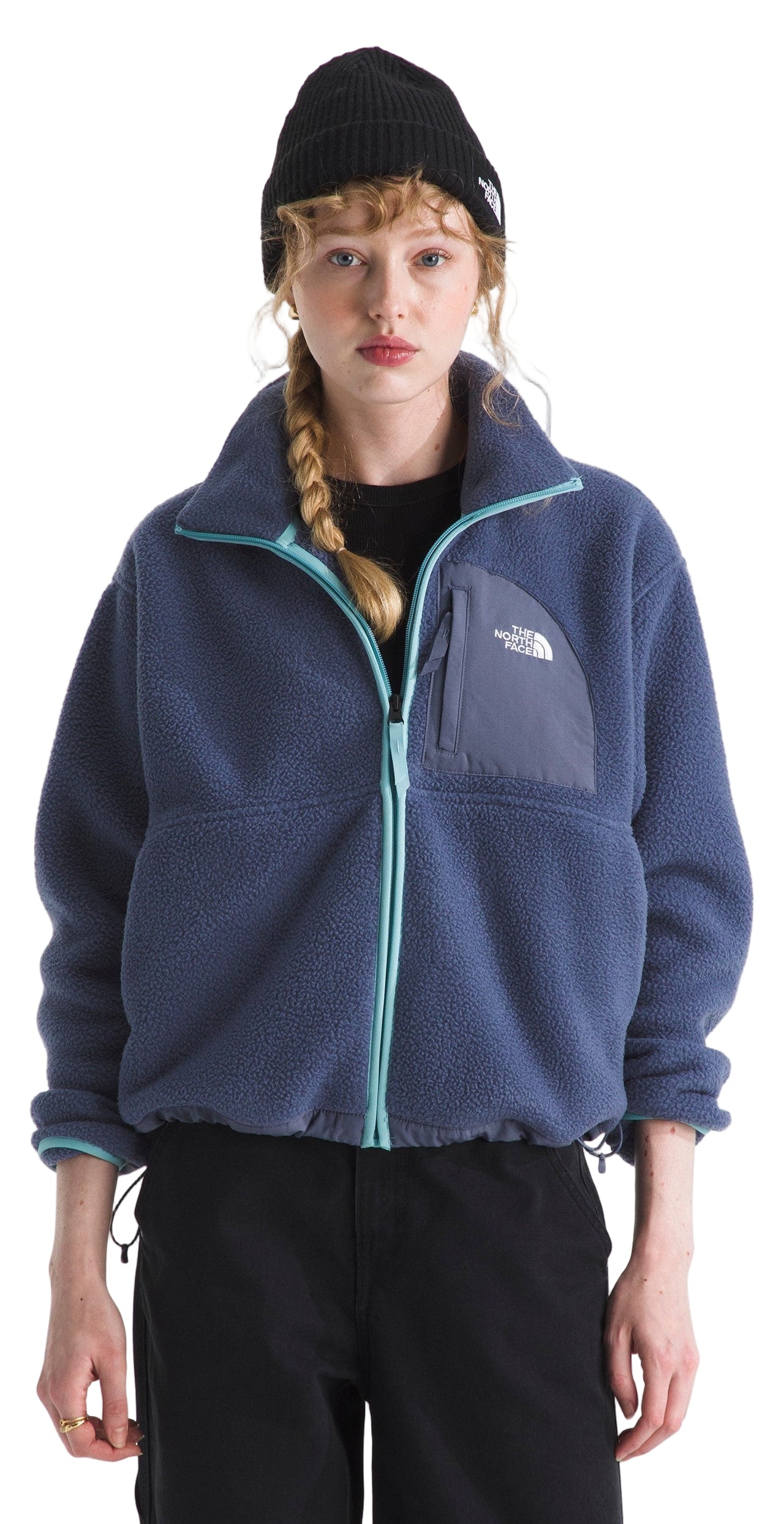 A woman wears a navy fleece jacket with teal accents, a black beanie, and black pants.