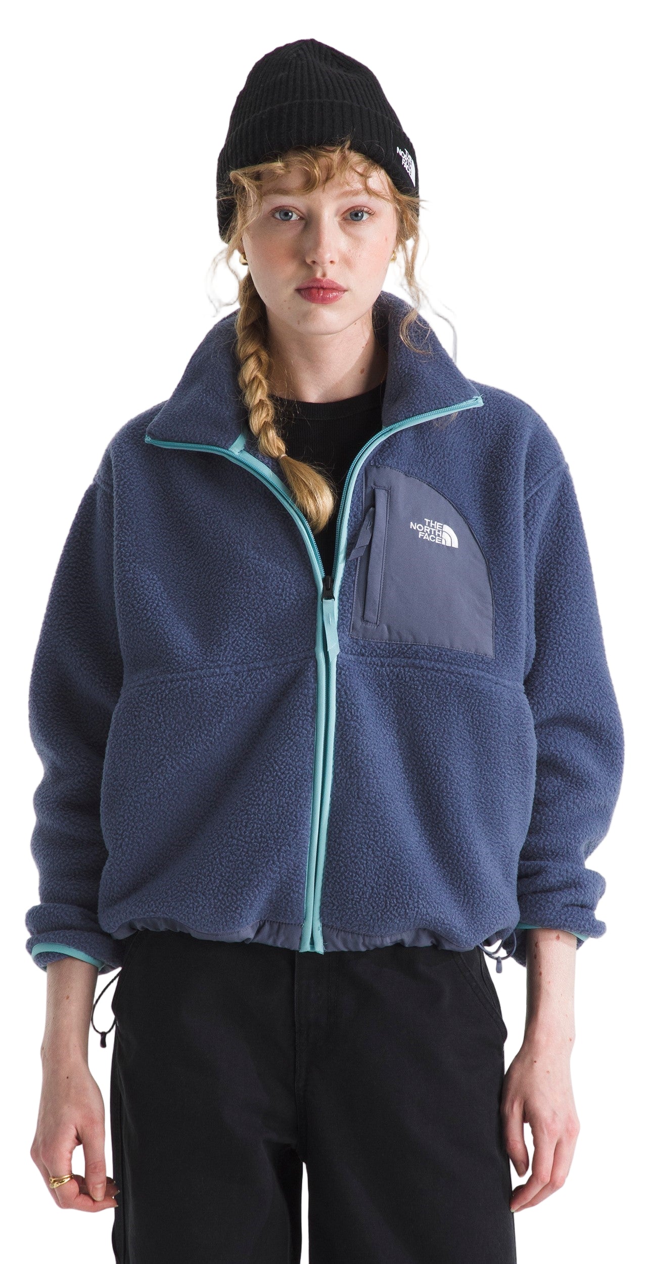 A woman wears a navy fleece jacket with teal accents, a black beanie, and black pants.
