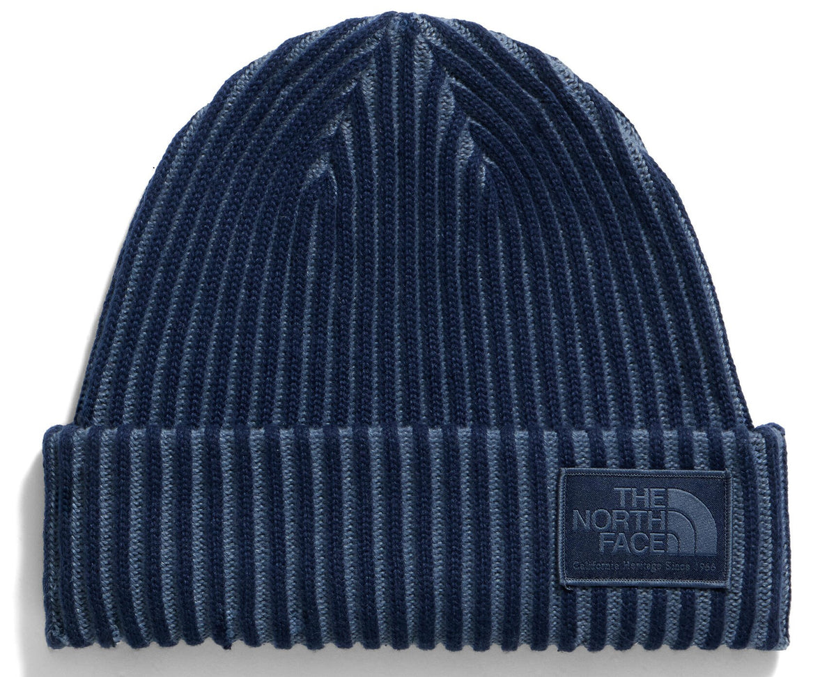 A dark blue and grey ribbed knit beanie with a rectangular patch on the front cuff featuring the text 'THE NORTH FACE' embossed in a matching dark color.
