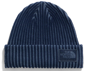 A dark blue and grey ribbed knit beanie with a rectangular patch on the front cuff featuring the text 'THE NORTH FACE' embossed in a matching dark color.