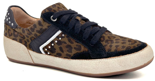A low-top sneaker with an animal print pattern on the upper, featuring black suede overlays, black laces, a light-colored textured midsole, and decorative silver studs along the side and heel tab.