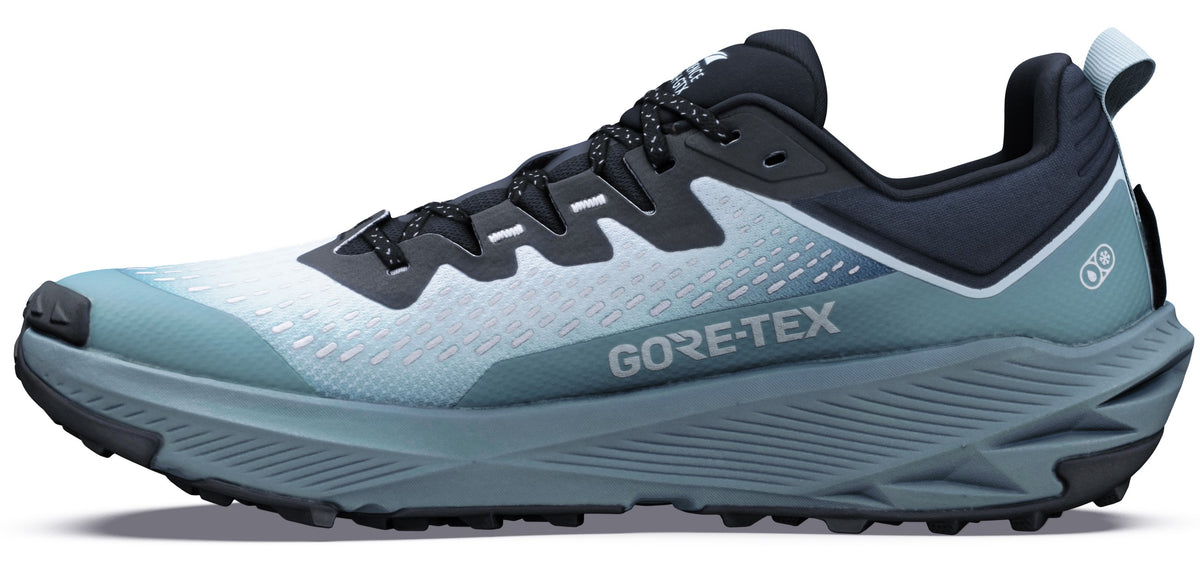 A low-top trail running shoe with a Gore-Tex membrane, featuring a white mesh forefoot that transitions into a muted seafoam green at the midfoot and heel, a thick dark grey midsole with a rugged textured pattern, and a black treaded outsole.