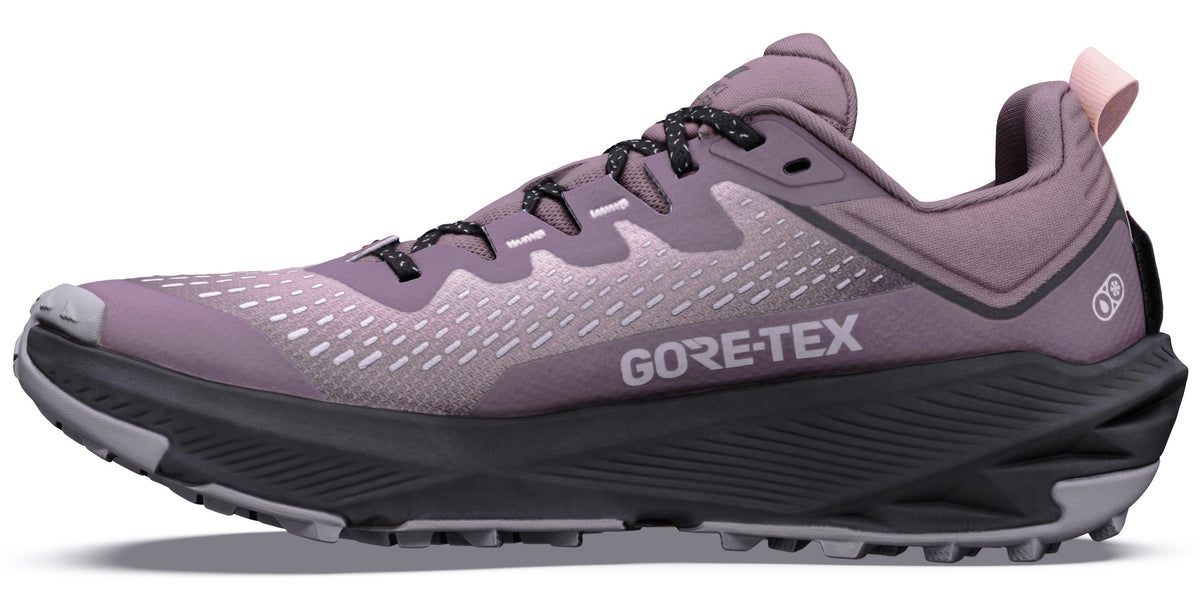 A side view of a mauve-colored trail running shoe with a dark grey, ridged midsole, black patterned laces, and the text GORE-TEX printed on the side.
