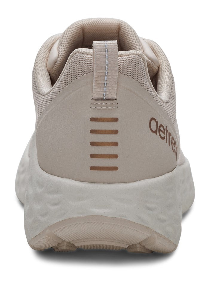 Back of beige-colored running shoe with textured sole and the text 'aetrex'.