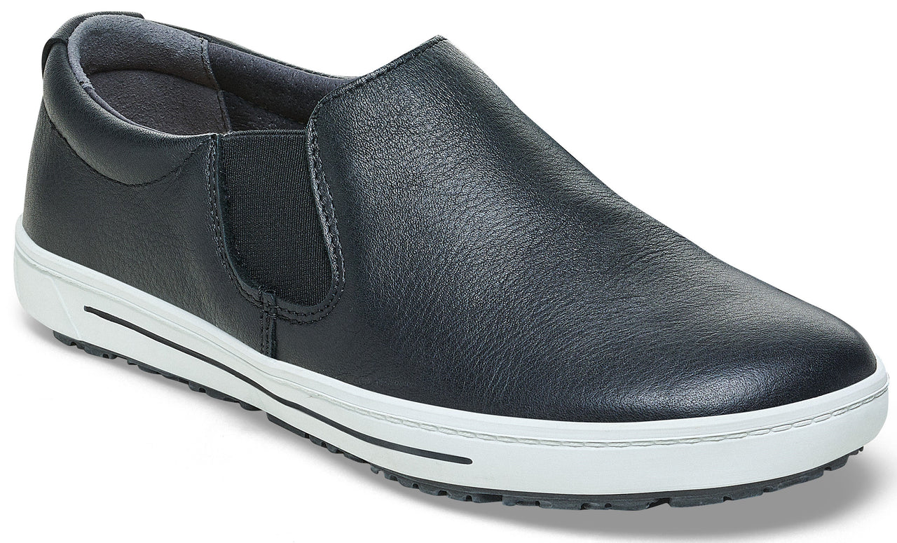 A black leather slip-on shoe with a thick white rubber midsole and black non-slip outsole, featuring side elastic panels for a flexible fit.