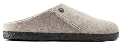 Side view of a beige felt slip-on slipper with a dark brown textured rubber sole and a small metallic circular emblem on the side.