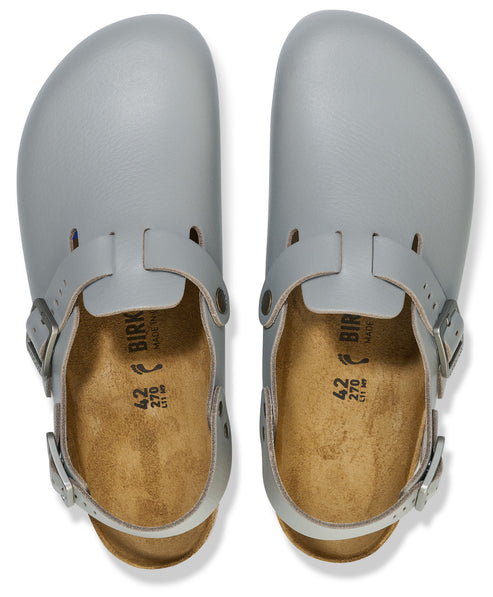 A pair of light gray, round-toed, backless clogs with buckled straps over the bridge and around the heel, featuring tan cork insoles with the text 'BIRK', '42', and '270' printed in black.