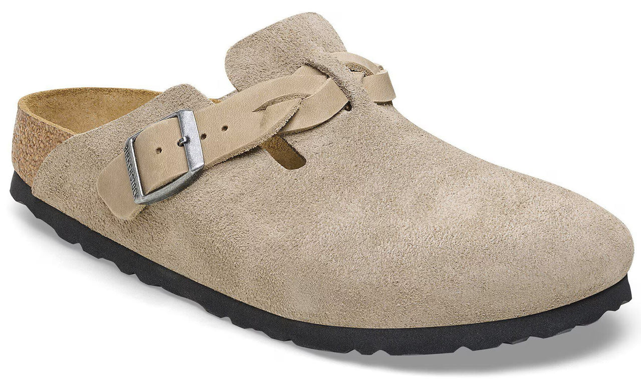 A beige suede clog-style shoe with a braided leather strap and an adjustable metal buckle across the instep, featuring a natural cork footbed and a textured black rubber sole.