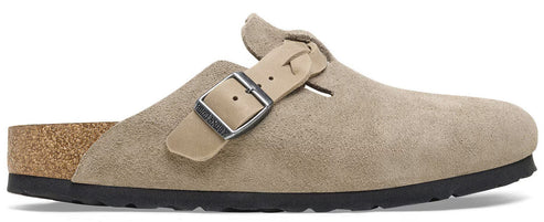 A beige suede slip-on clog with a cork footbed, a black sole, and a silver metal buckle strap across the side.